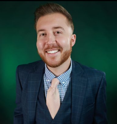 Smiling man in a suit with a tie against a green background.