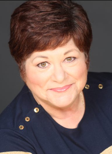 Headshot of a woman with short brown hair, smiling, wearing a dark top.